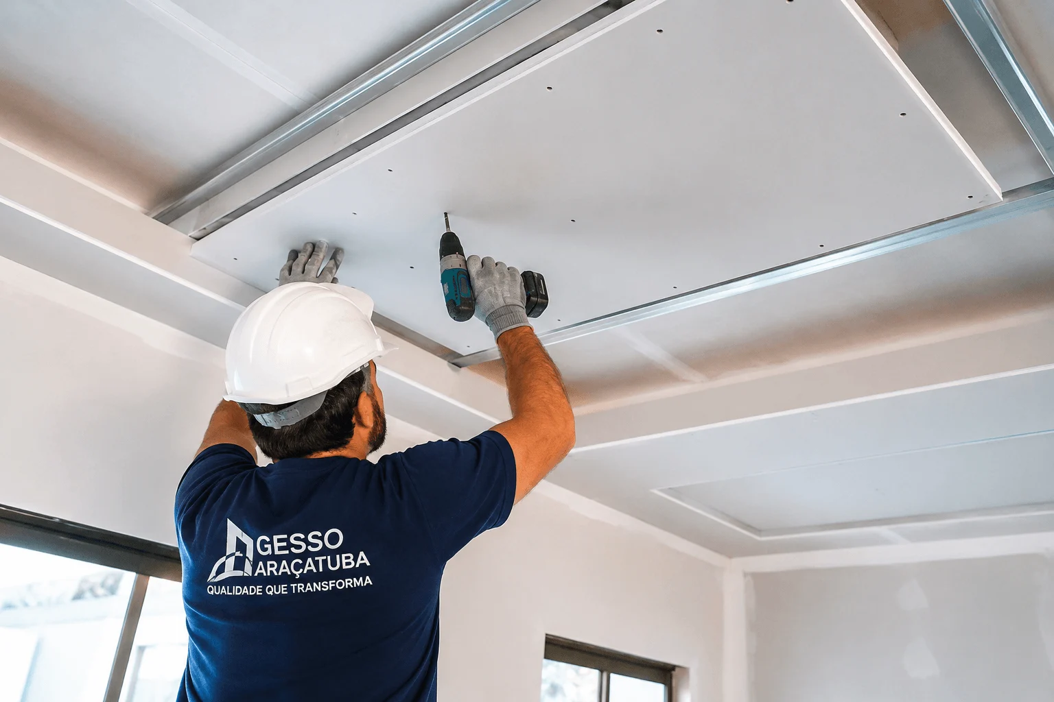 Gesseiro com camiseta azul marinho instalando forro de gesso em Andradina com estrutura de drywall no teto